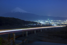 高速道路の向こうに富士市内の明かりと富士山のシルエットが浮かぶ