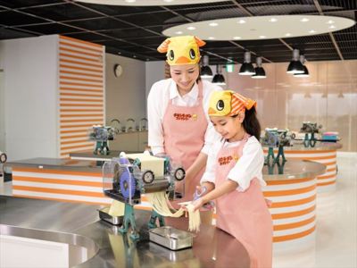 「チキンラーメンファクトリー」では、製麺機で生地を薄く延ばしたら、麺状に切り出して約20cmの長さにカットする(体験はペア)