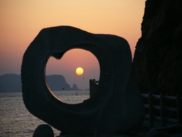 石のモニュメント「波の詩(うた)」越しに太陽を眺める